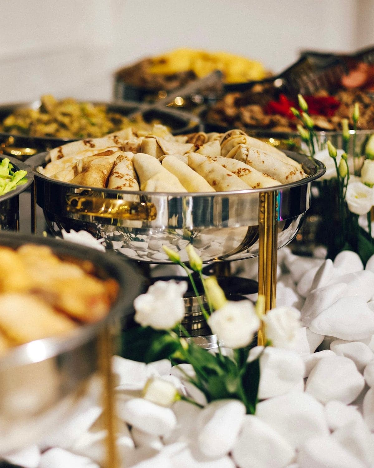 Buffet von AHUEVENT: gefüllte Teigrollen in einer Chafing Dish, dahinter Salate und warme Speisen