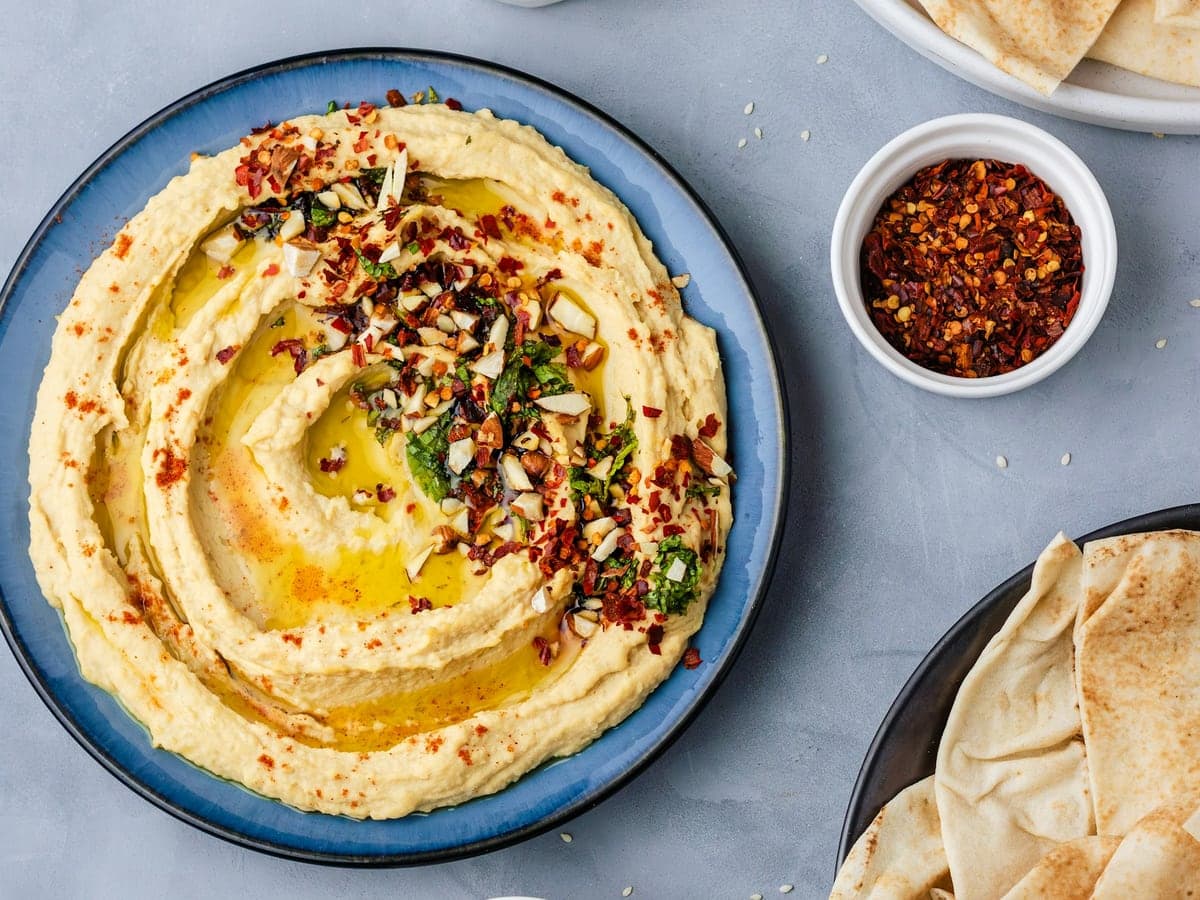 Schale Hummus mit Olivenöl und Gewürzen, daneben Fladenbrot
