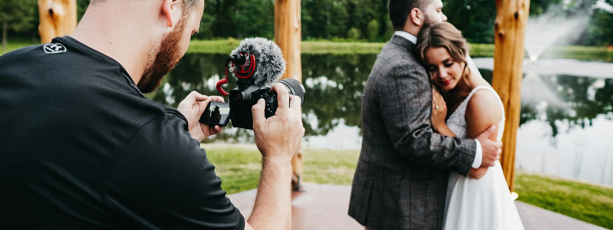 Videograf filmt ein Brautpaar mit Kamera und Richtmikrofon, das Paar umarmt sich im Abendlicht