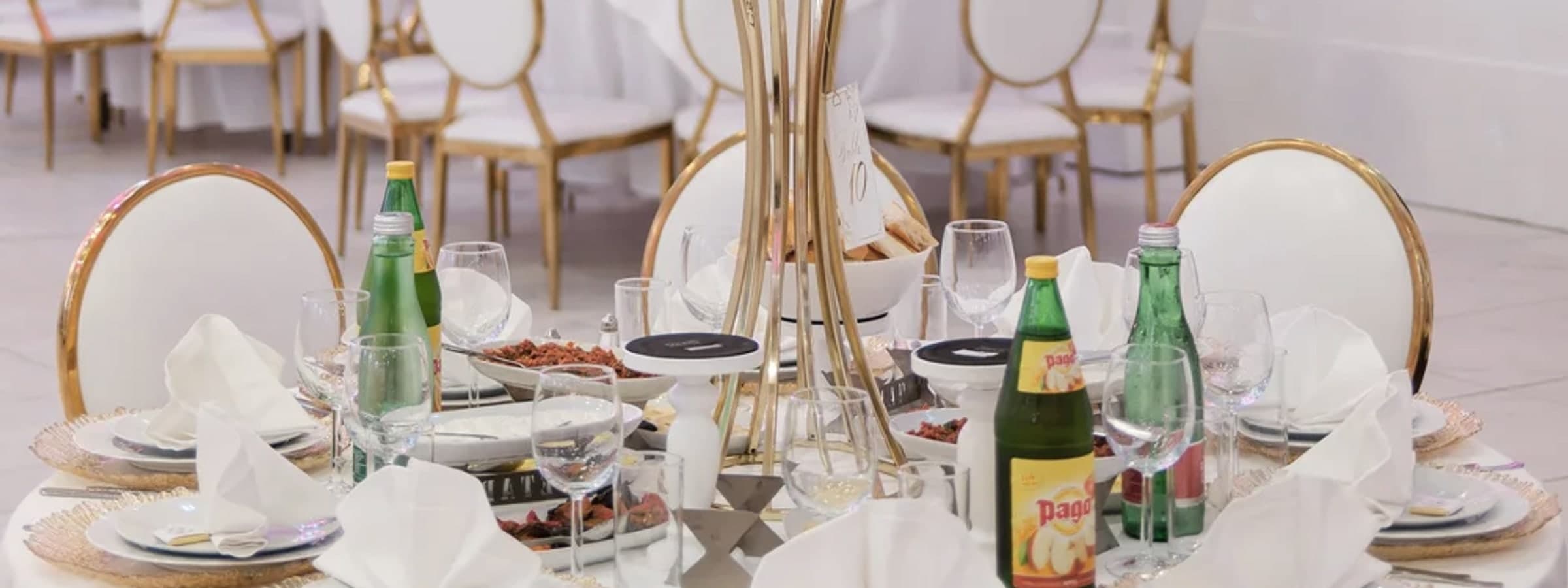 Gedeckte Tafel im Saal von AHUEVENT mit goldgerandeten Platztellern, Gläsern und gefalteten Stoffservietten